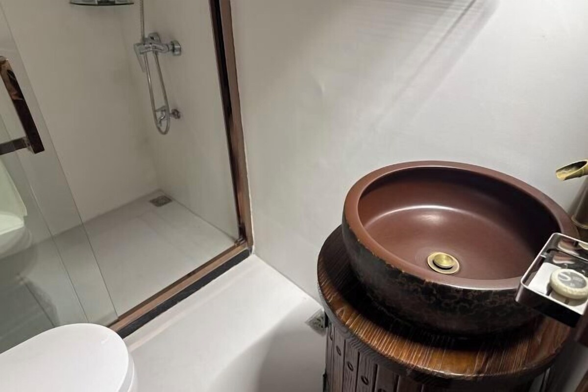 Een badkamer met een rond, bruin wastafel op een houten voetstuk, een douchecabine met glazen wanden, en een wit toilet.