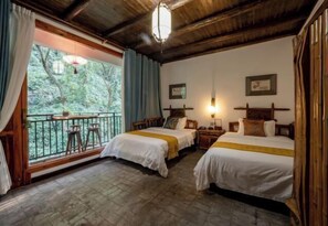 Relax on the balcony with a view of lush greenery, featuring two beds and a table for two.