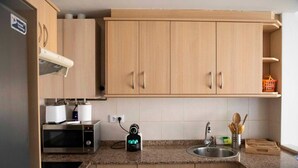 Une cuisine équipée de meubles en bois, d’un four à micro-ondes, d’une bouilloire et d’un évier avec des ustensiles.