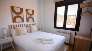 Une chambre bien rangée, avec un grand lit, deux tables de chevet avec des lampes, un radiateur et une fenêtre donnant sur la campagne.