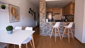 Une cuisine moderne avec des meubles en bois et un pare-feu en pierre, un coin repas avec une table et des chaises blanches, et une petite plante en pot posée sur la table.