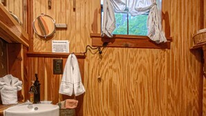Un baño de madera con lavamanos, inodoro y ventana con cortinas.