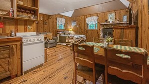 Interior acogedor de una cabaña con paredes y detalles de madera, una mesa de comedor, sillas, un sofá, una chimenea y una cocina con estufa y armarios.