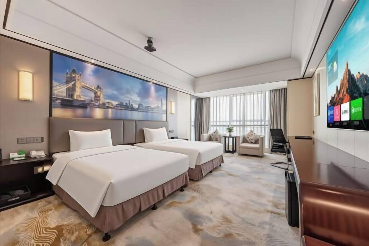 A hotel room with two beds, a large TV, a desk, and a view of a bridge.