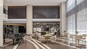A spacious lobby with a grand piano, seating area, and a modern staircase.