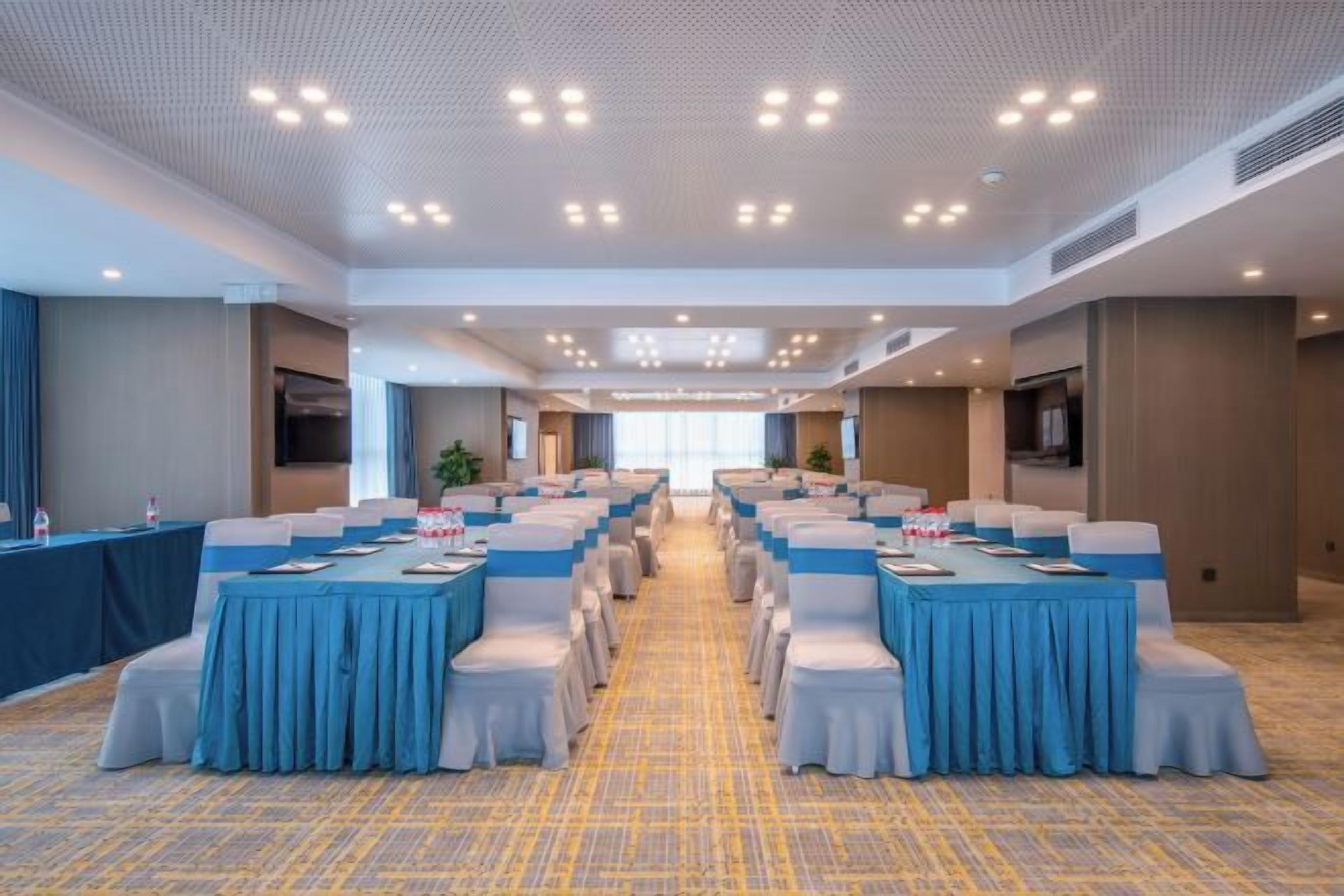 Un salón de conferencias con varias mesas y sillas, piso alfombrado e iluminación empotrada en el techo.