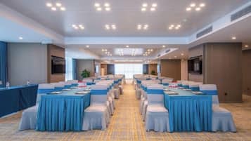 Un salón de conferencias con varias mesas y sillas, piso alfombrado e iluminación empotrada en el techo.