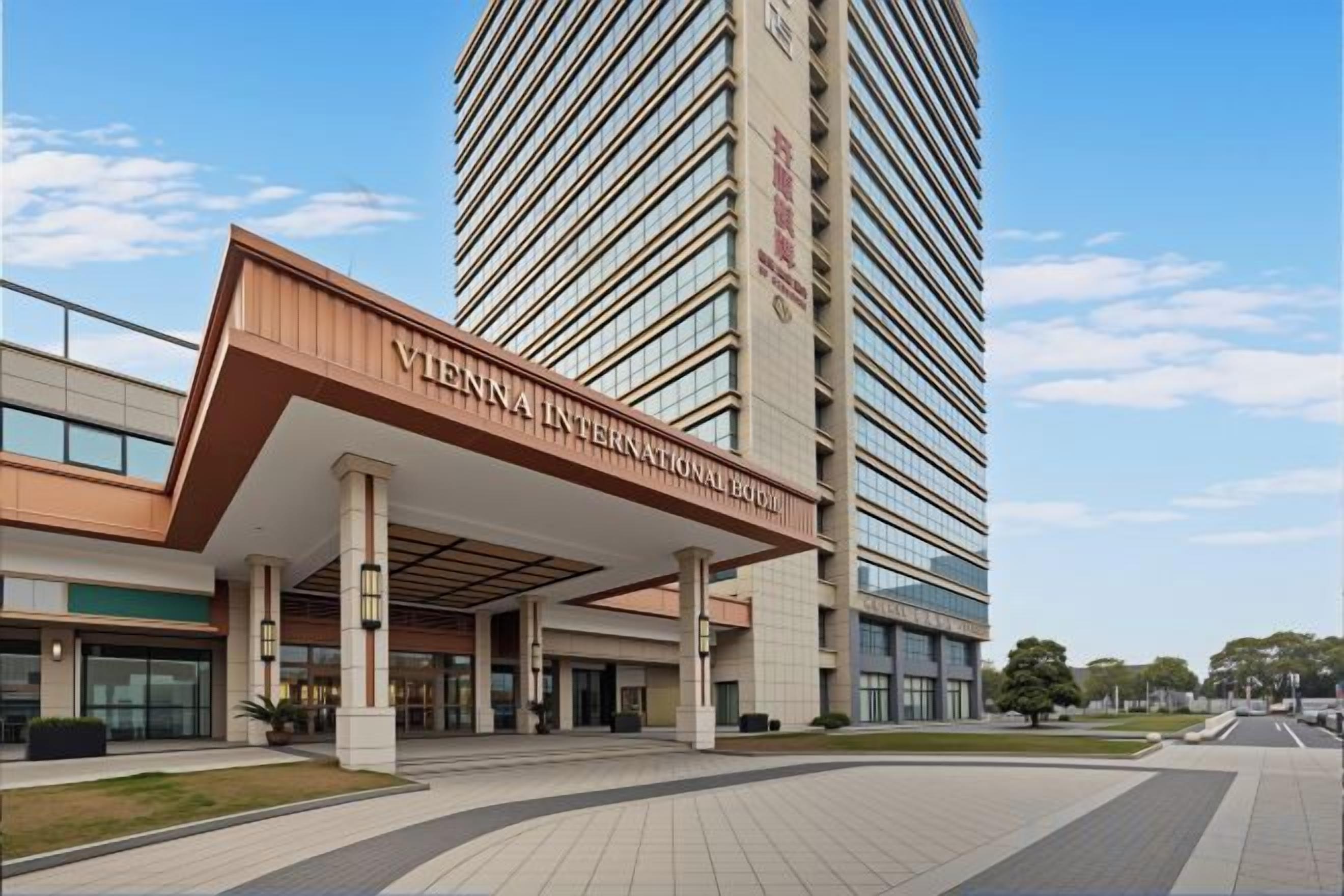 Un hotel moderno con una entrada destacada, un edificio alto al fondo y un cielo despejado.