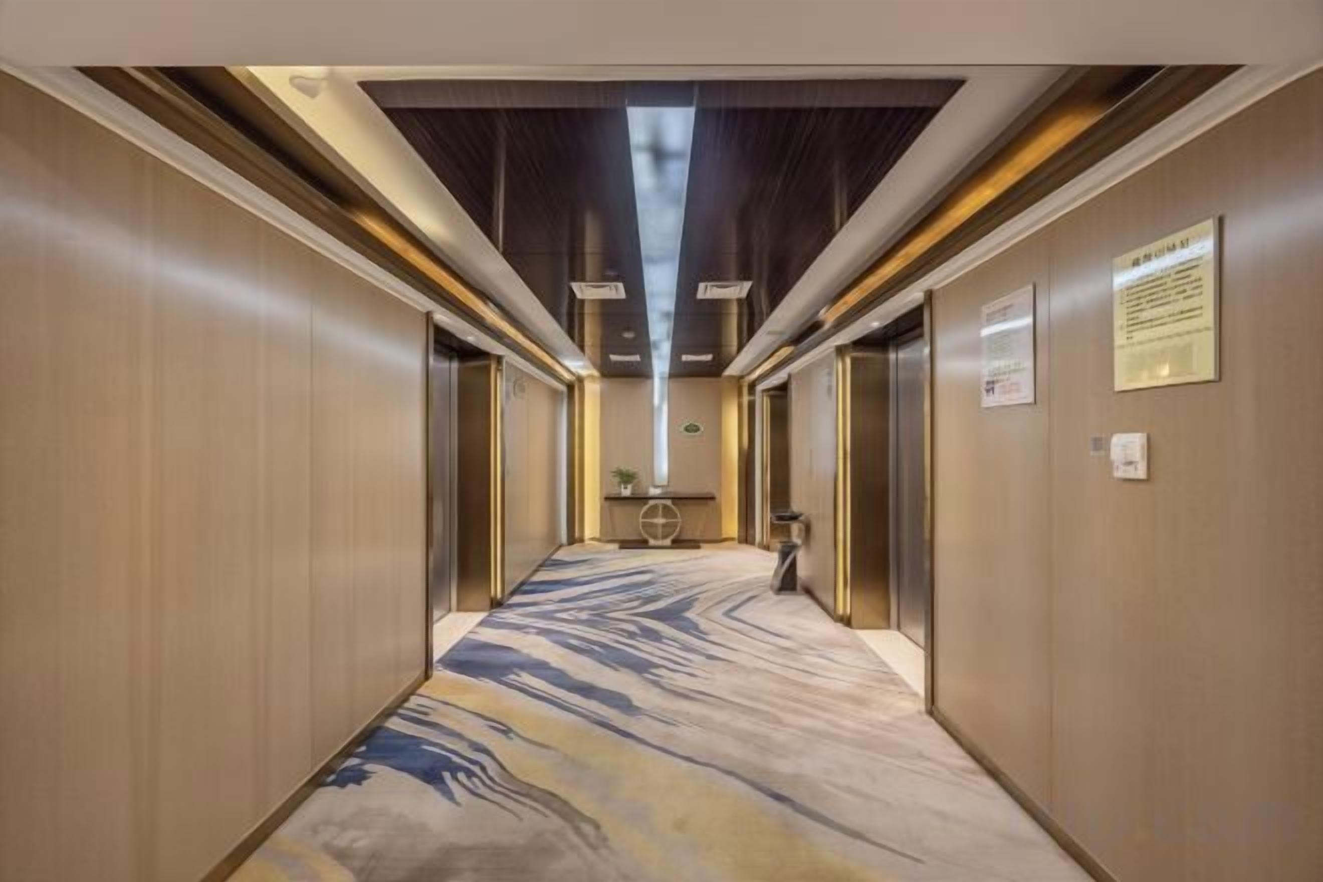 Un pasillo de hotel con alfombra de diseño de mármol, un ascensor central y un mostrador de recepción.