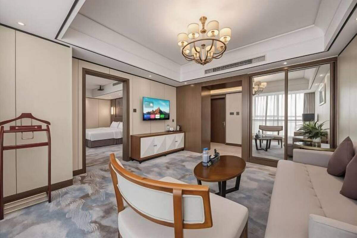 A hotel room with a bed, a TV, a desk, a sofa, and a chandelier.