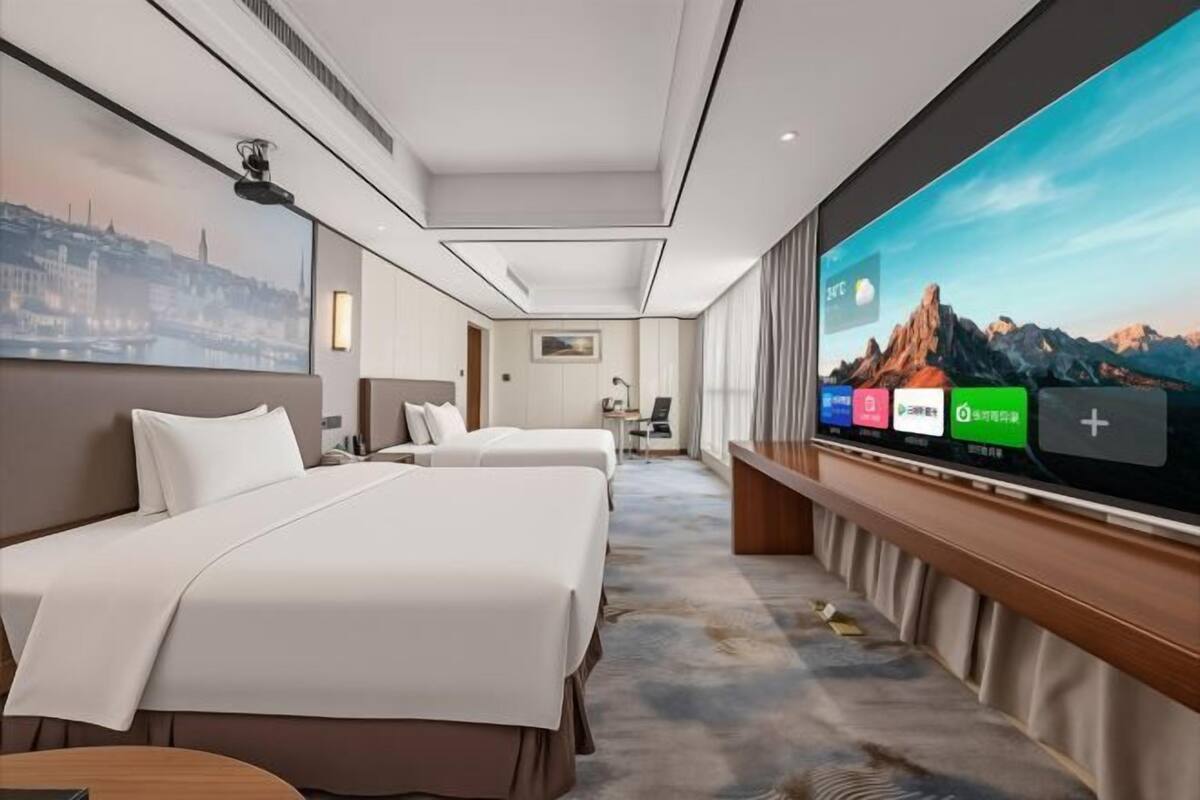 A hotel room with two beds, a large TV, and a cityscape painting on the wall.