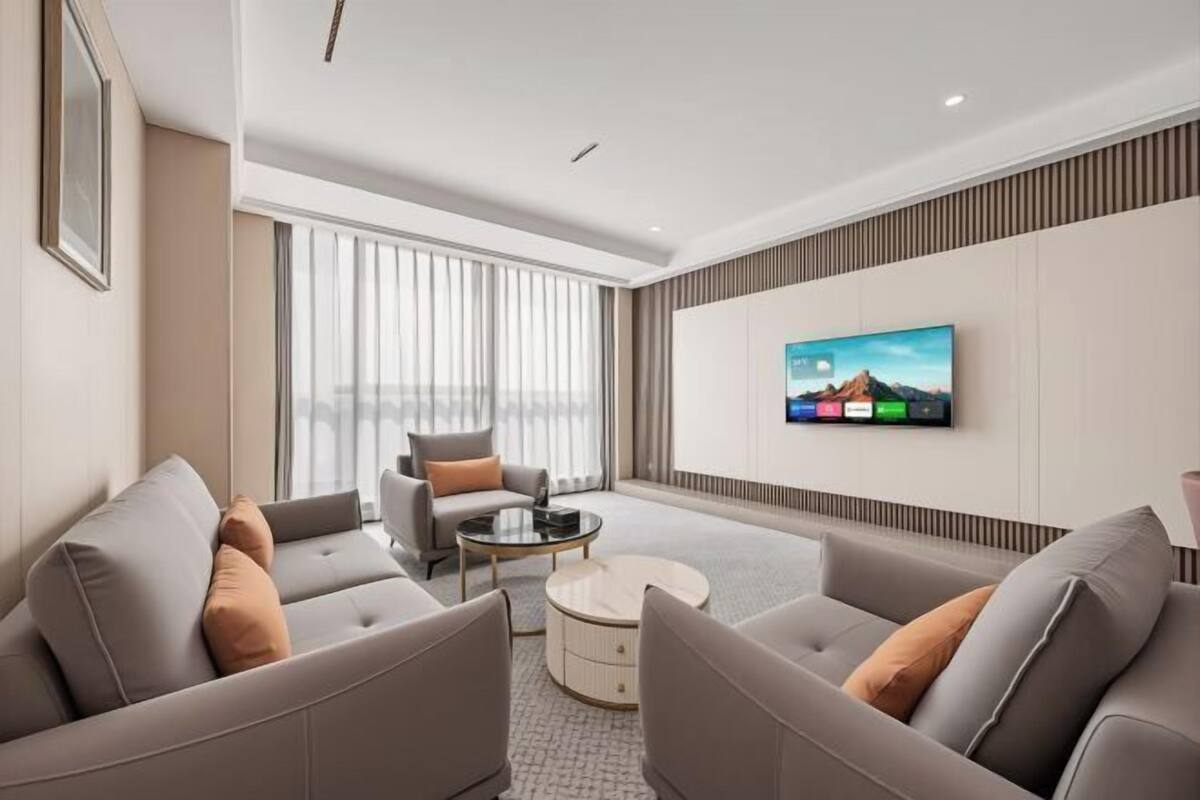 A modern living room with a flat-screen TV, a sofa set, a coffee table, and a large window with curtains.