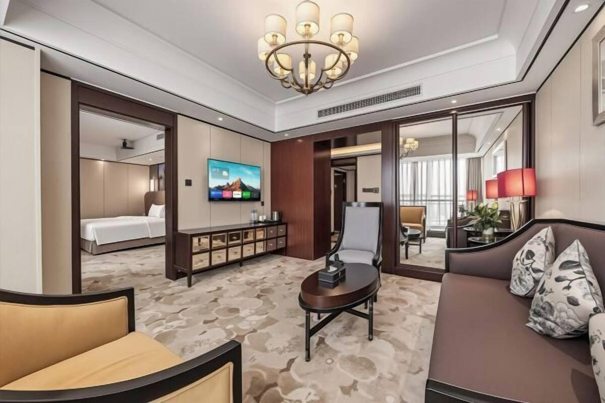 A hotel room with a bed, a TV, a sofa, a small table, and a mirror.