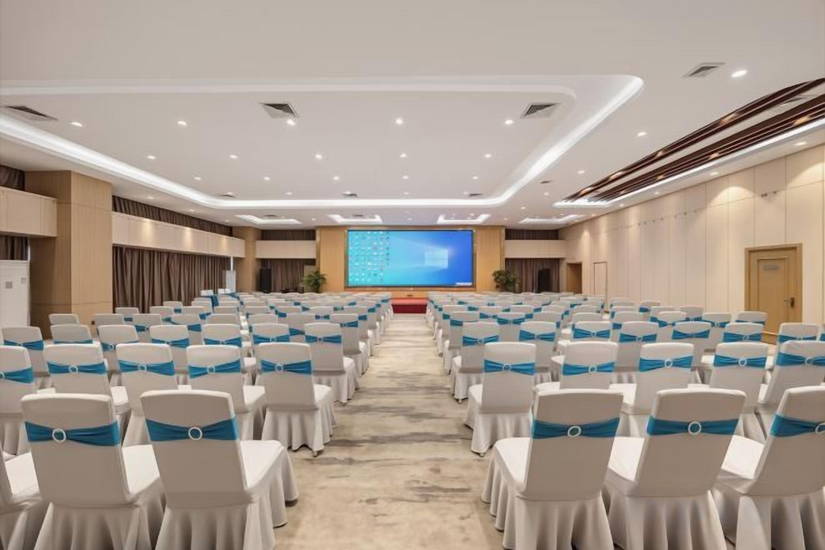 A conference room with rows of chairs, a stage with a screen, and a carpeted floor.