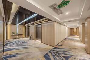 A hotel corridor with a patterned carpet, elevators, and a reception area with a plant. - Hangzhou Yuecheng Audio & Video International Hotel (Boao Xinhan Road Subway Station) (Hangzhou)