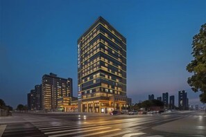 A multi-story hotel with a modern design, featuring a prominent corner location with a wide street view. - Hangzhou Yuecheng Audio & Video International Hotel (Boao Xinhan Road Subway Station) (Hangzhou)
