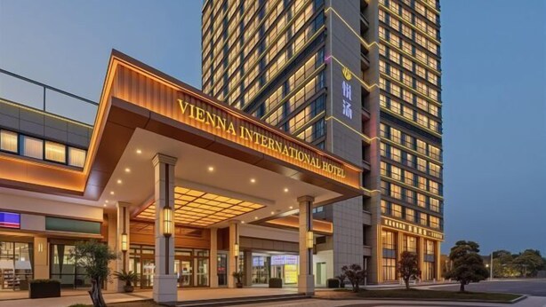 A modern hotel entrance with a prominent sign, a covered walkway, and a tall building in the background.