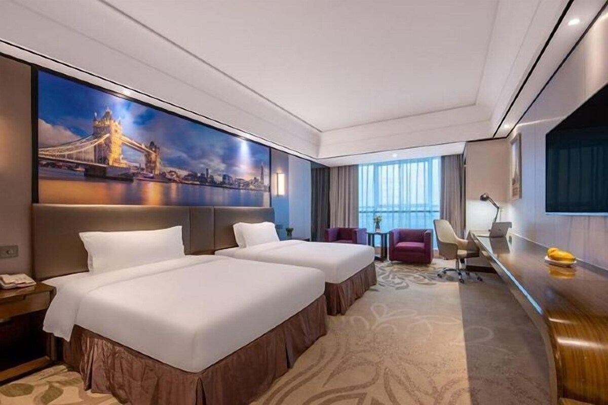 Ein Hotelzimmer mit zwei Betten, einem Schreibtisch, einem Sessel, einem Fernseher und einem großen Fenster.