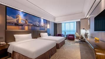 A hotel room with two beds, a desk, a chair, a TV, and a large window.