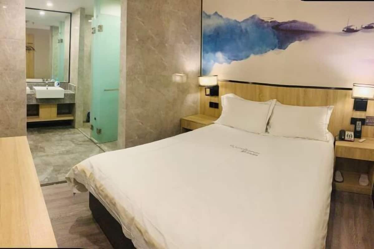 A hotel room with a bed, nightstands, a painting, and a bathroom visible through an open door.