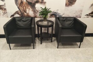 Two black leather armchairs and a small round table with a potted plant in a room with a tiled floor. - Qingmu Hotel (Nanjing Xinzhuang Metro Station) (Nanjing)