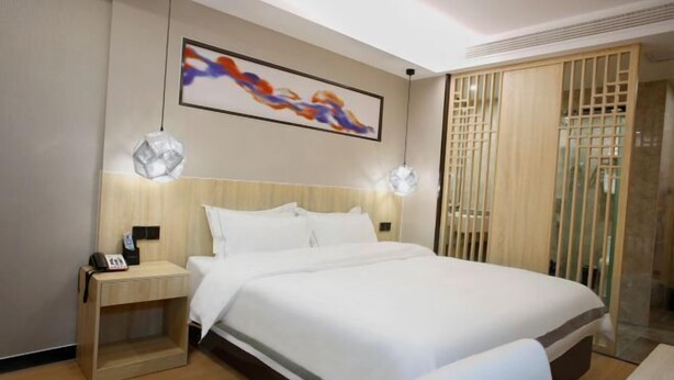 A hotel room with a large bed, a bedside table with a phone, a wall-mounted artwork, and a wooden partition. - Qingmu Hotel (Nanjing Xinzhuang Metro Station) (Nanjing)