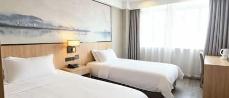 Habitación de hotel con dos camas, un escritorio, una silla, una lámpara y un cuadro en la pared.