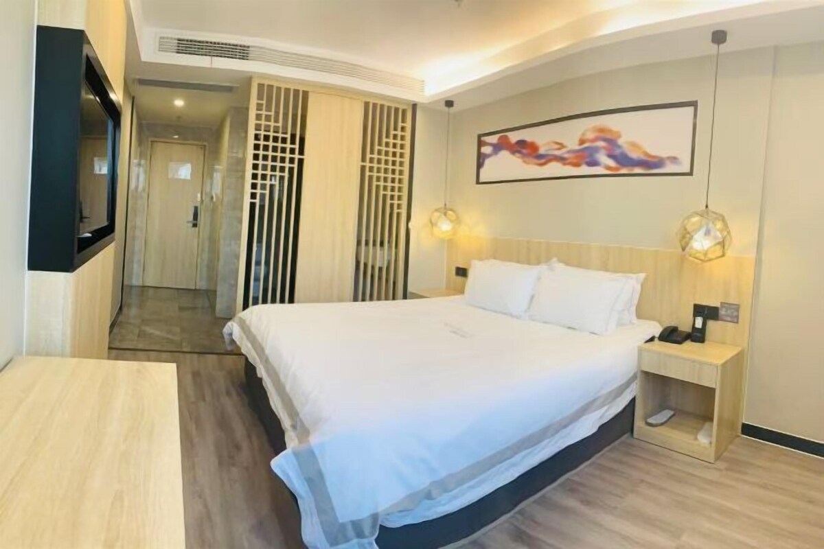 A hotel room with a bed, bedside table, and a TV mounted on the wall.
