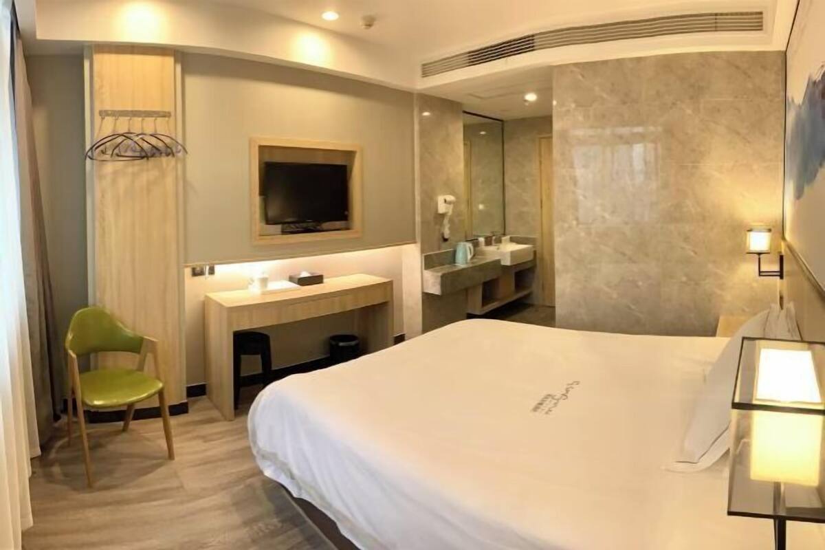 A hotel room with a bed, a desk, a chair, a TV, a mirror, and a bathroom.