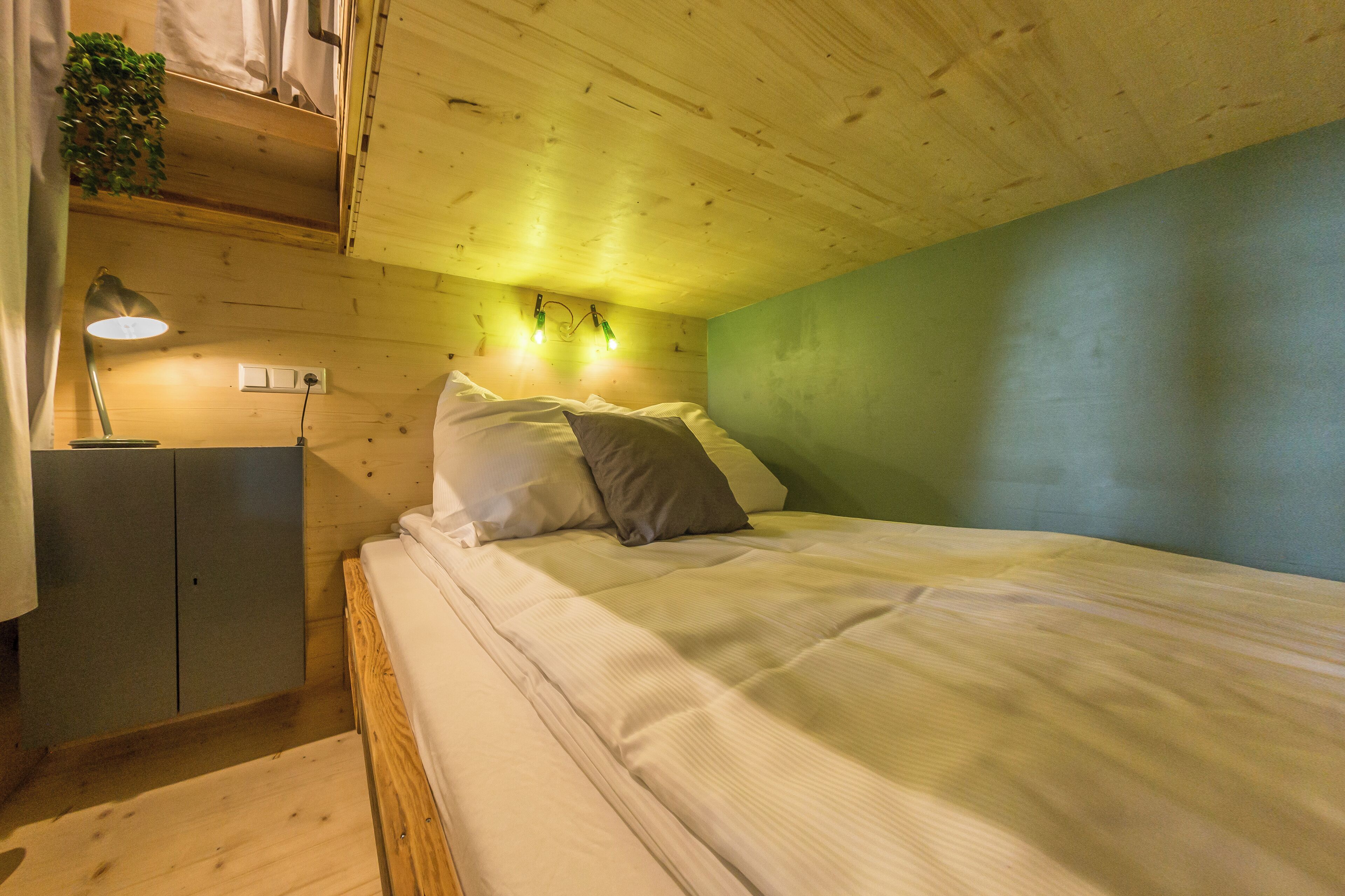A bedroom with a wooden ceiling, a bed with white bedding, a nightstand with a lamp, and a green wall.