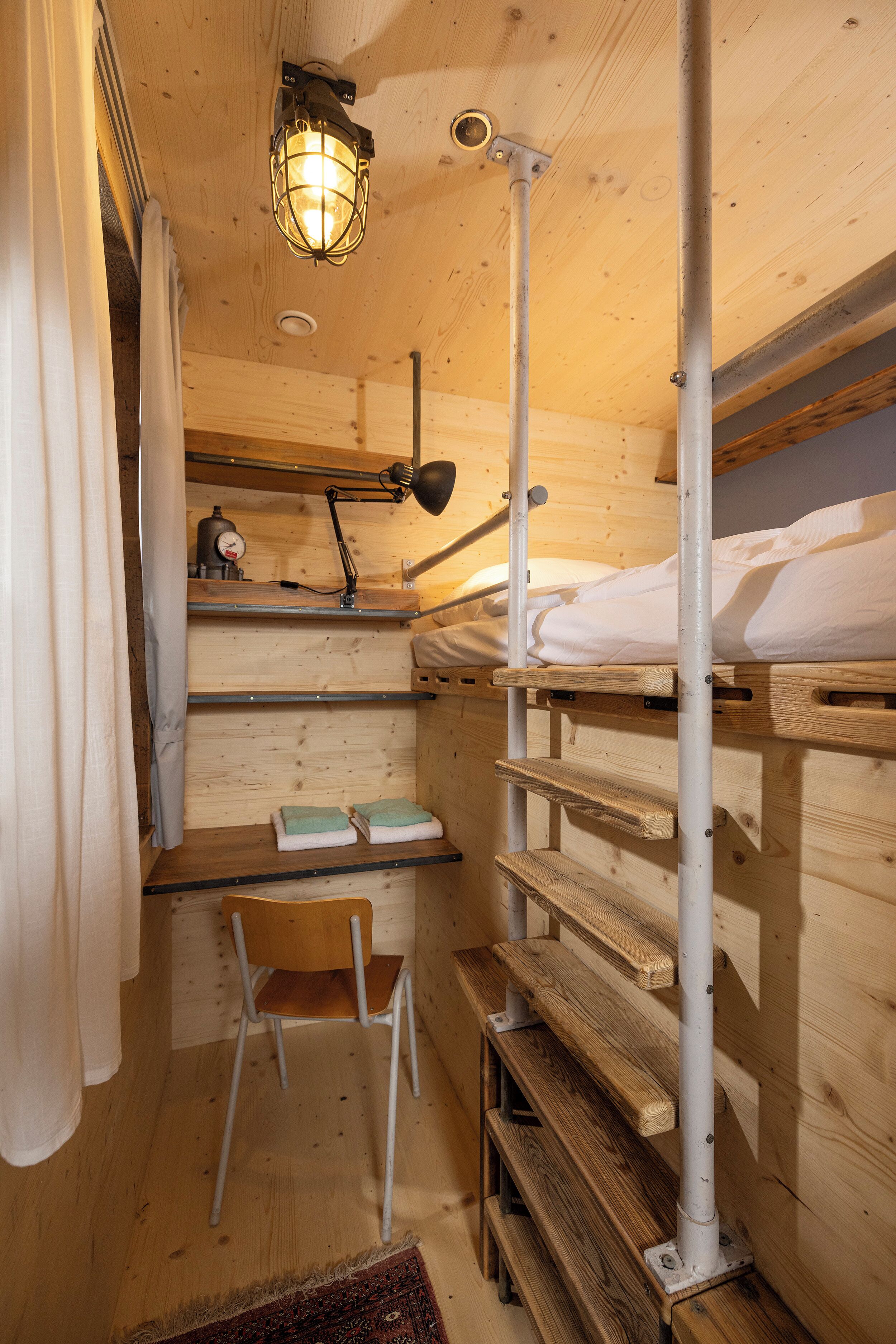 Interior de una cabaña de madera con literas, un escritorio, una silla y una lámpara de escritorio.
