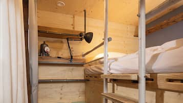 Interior de una cabaña de madera con literas, un escritorio, una silla y una lámpara de escritorio.