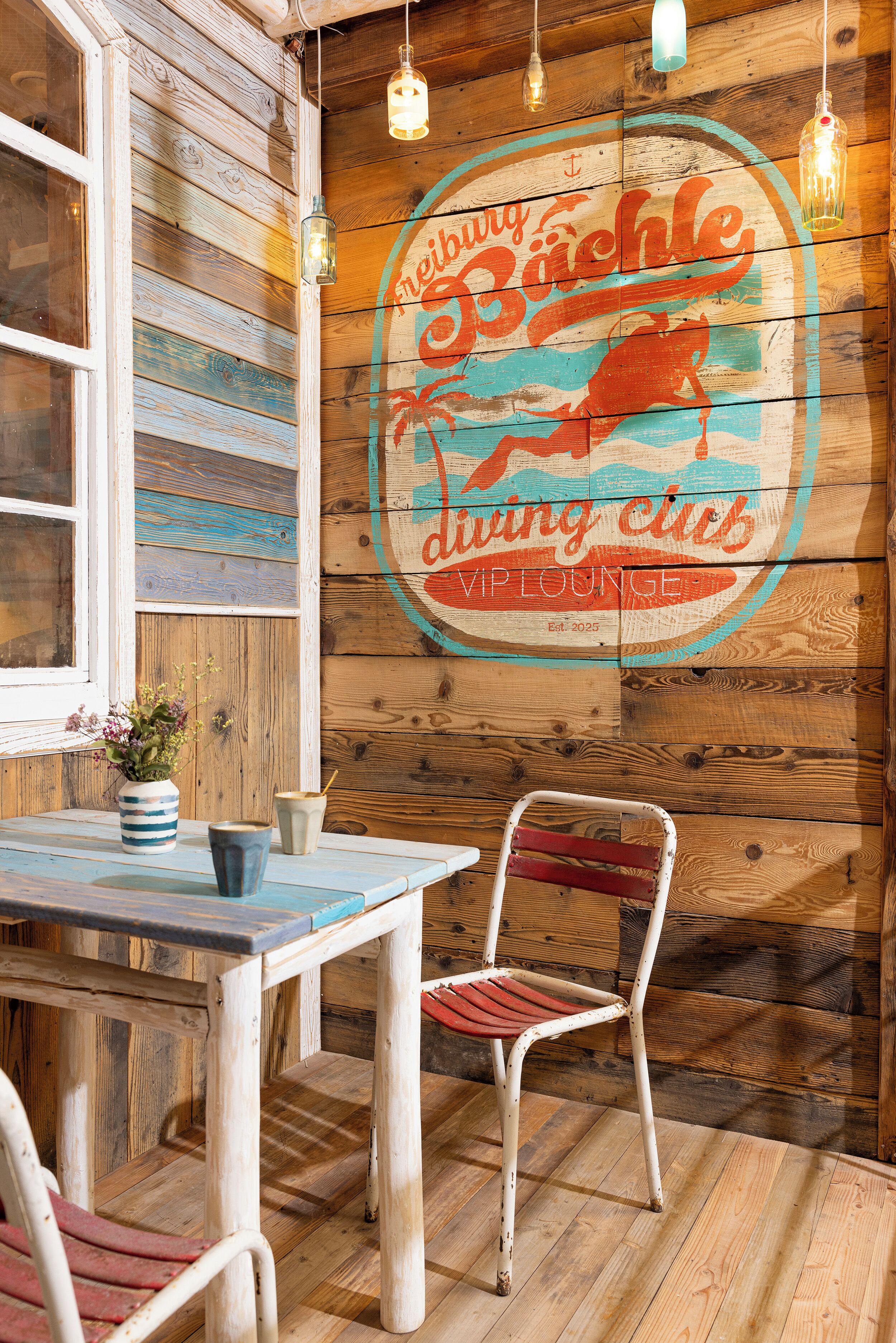 Ein Holzinterieur mit einem Tisch, Stühlen und einem Wandschild mit der Aufschrift "Bächte diving club".