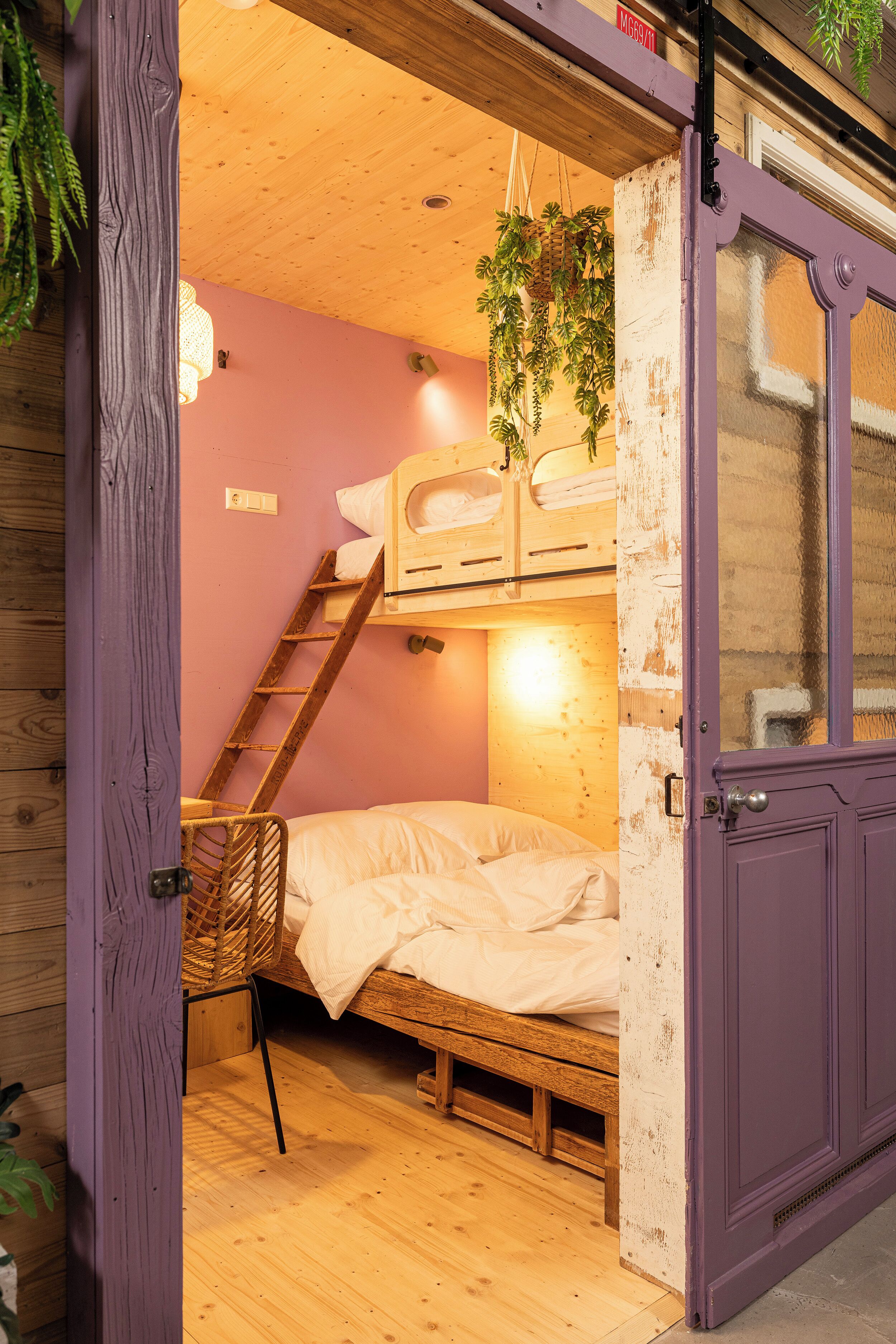 Habitación pequeña con literas, piso de madera y una puerta morada.