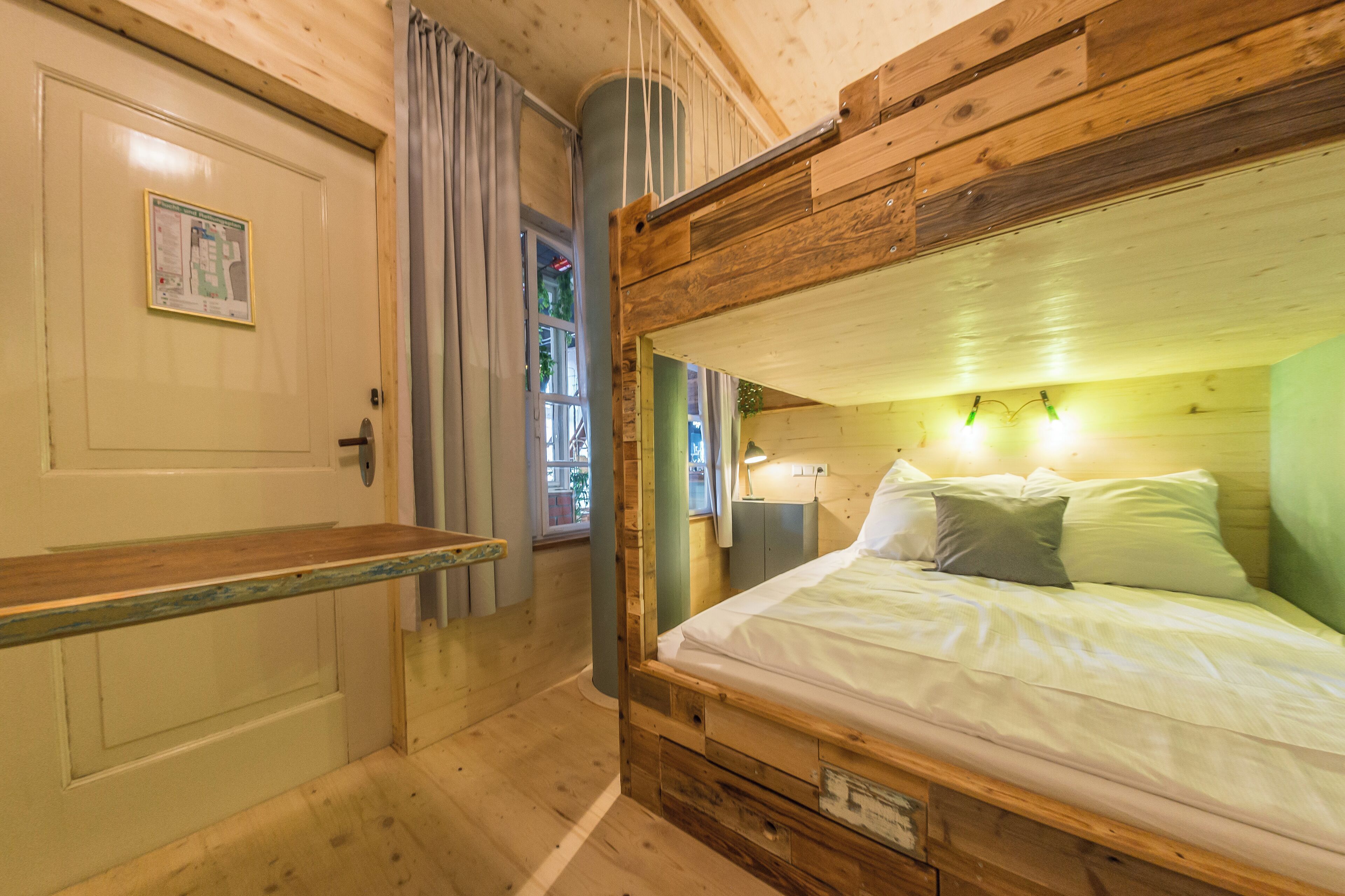 Un lit superposé en bois, avec une tête de lit, une table de chevet et une fenêtre avec des rideaux.