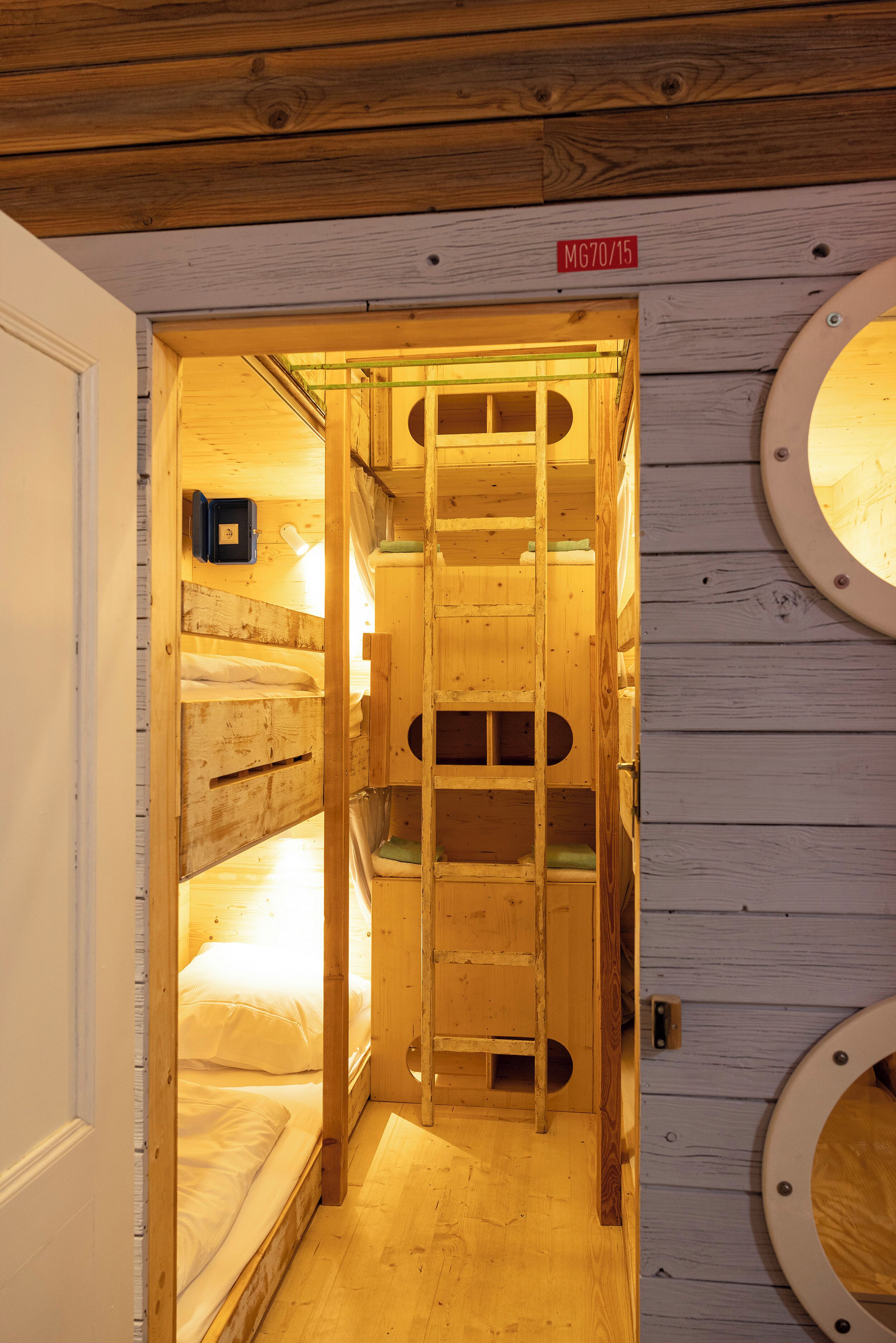 A wooden interior with a bunk bed, a circular window, and a door with a sign.