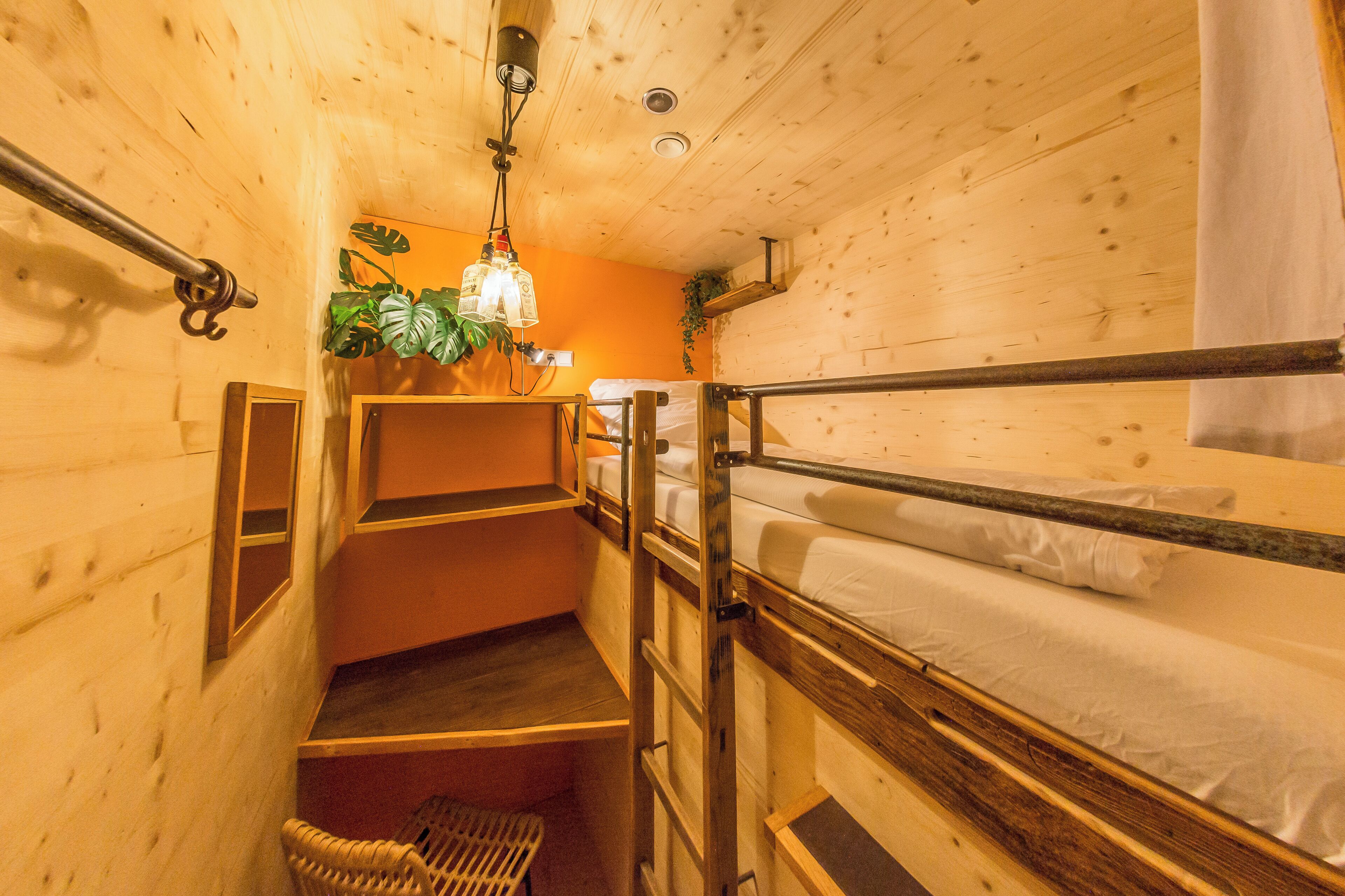 A wooden cabin-style room with bunk beds, a small staircase, and a hanging light fixture.