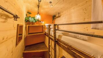 A wooden cabin-style room with bunk beds, a small staircase, and a hanging light fixture.