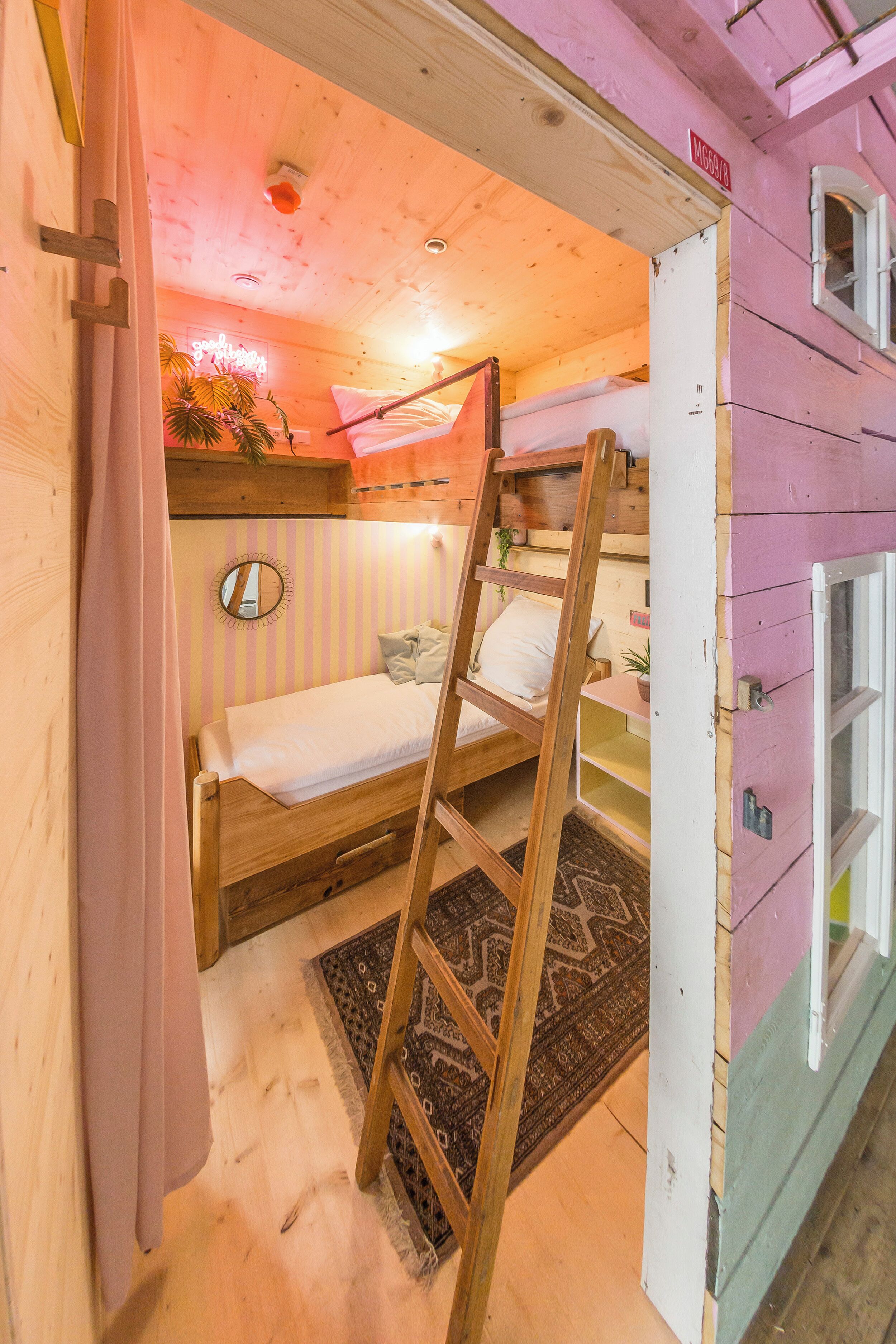 A cozy room with a bunk bed, a ladder, a mirror, and a small table with a plant.