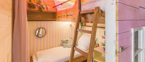 A cozy room with a bunk bed, a ladder, a mirror, and a small table with a plant.