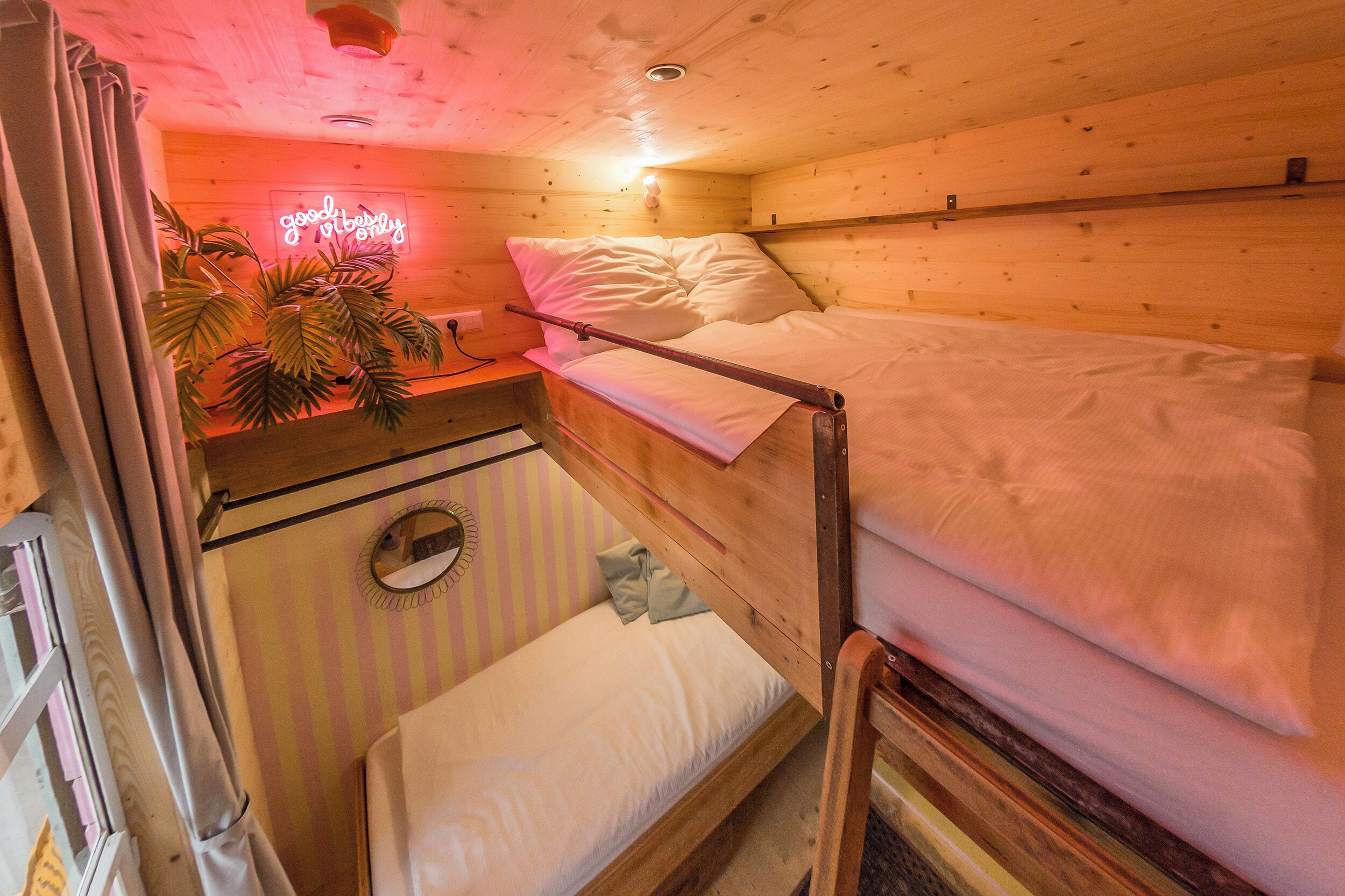 A cozy cabin room with a bunk bed, a small desk with a neon sign, and a potted plant.