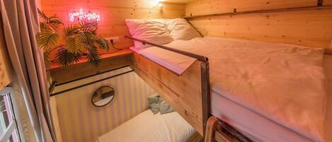 A cozy cabin room with a bunk bed, a small desk with a neon sign, and a potted plant.