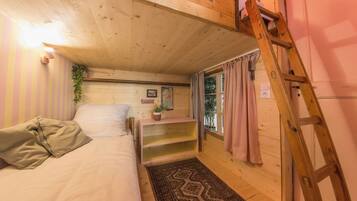 Une chambre à coucher accueillante, avec un lit, une échelle en bois, une étagère avec une plante et une fenêtre avec des rideaux.