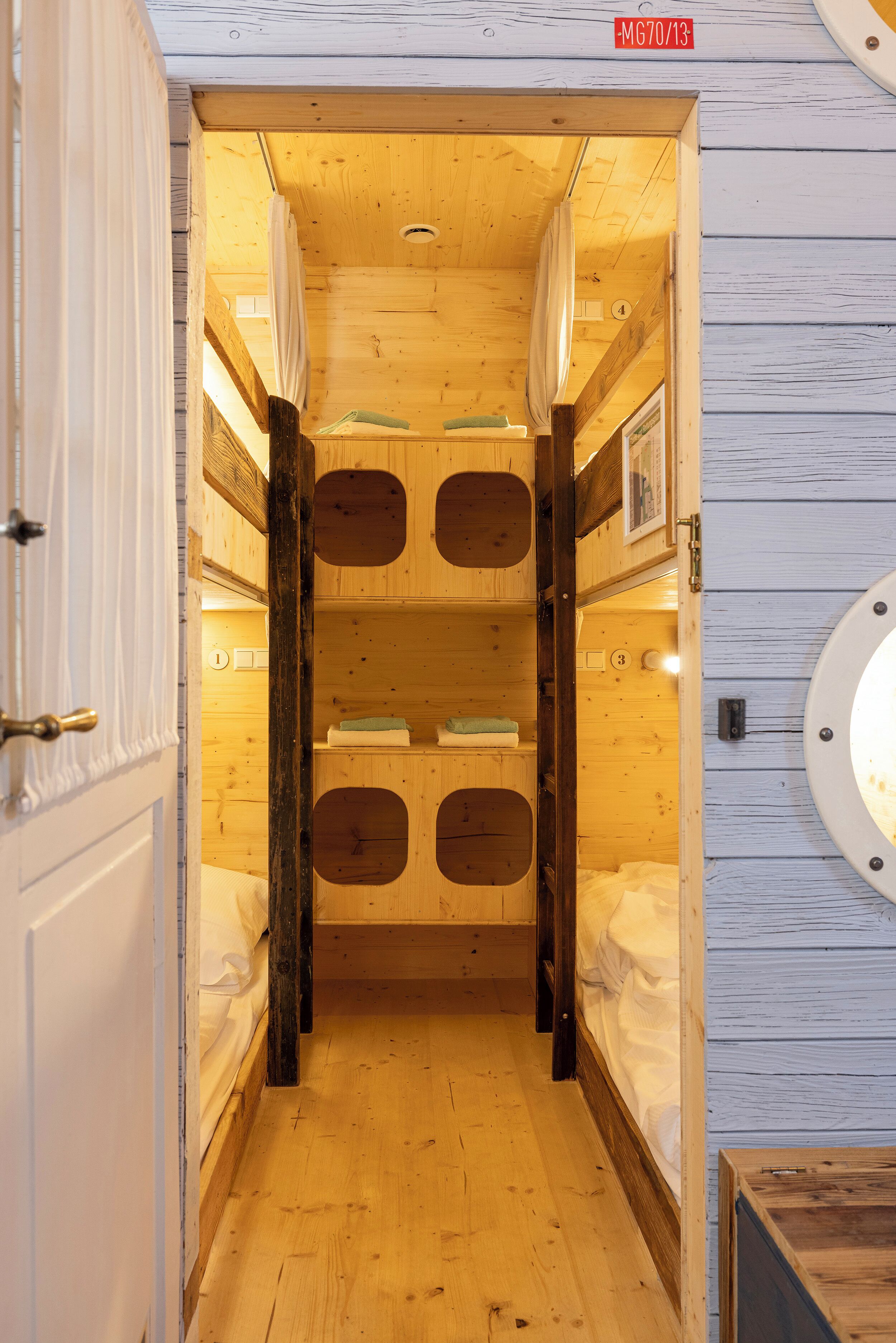 A narrow wooden hallway with bunk beds and a circular window on the right wall.