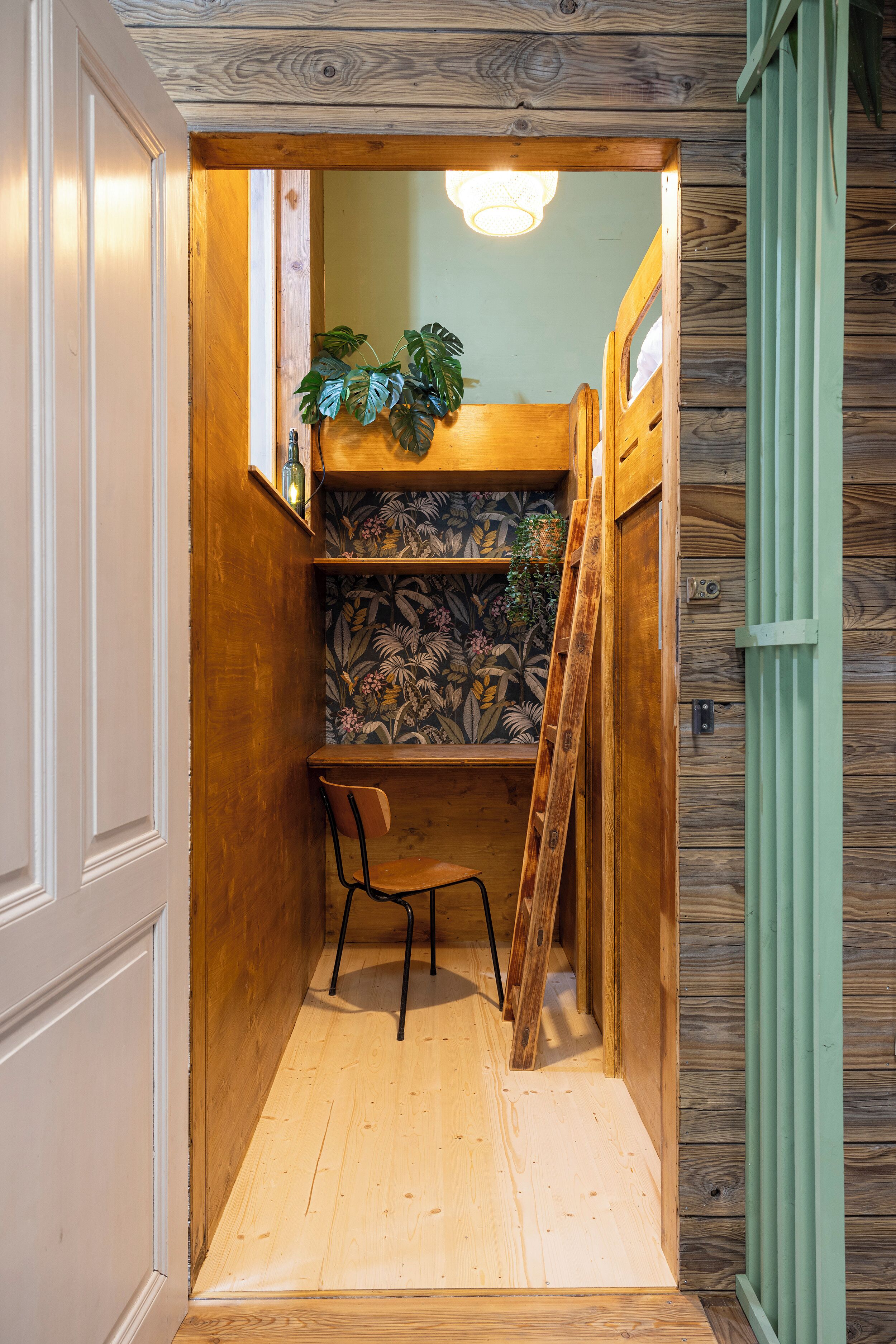 Habitación de madera estrecha con un escritorio, una silla y una escalera.