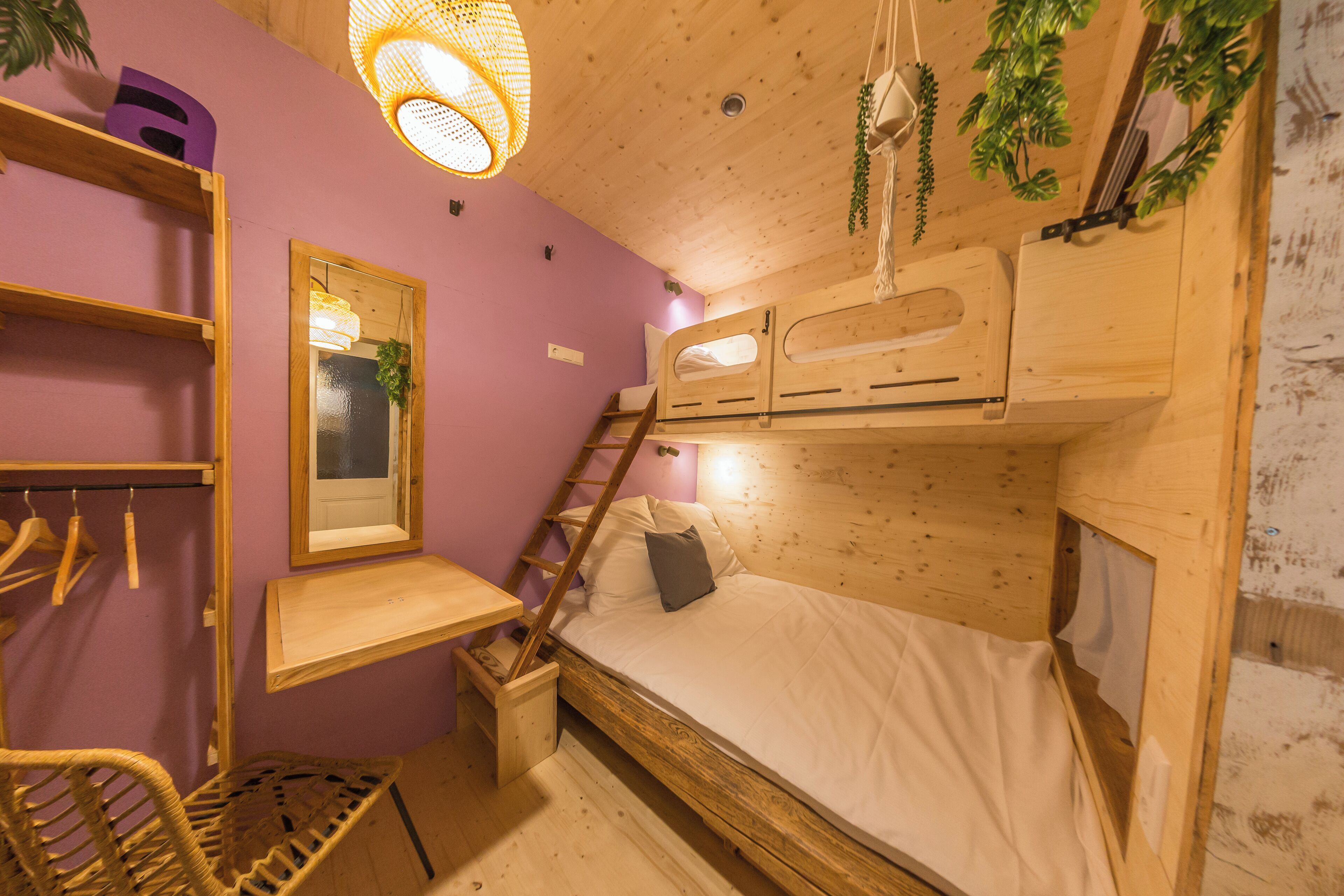 A compact room with a bunk bed, a wooden desk, a chair, and a hanging light fixture.