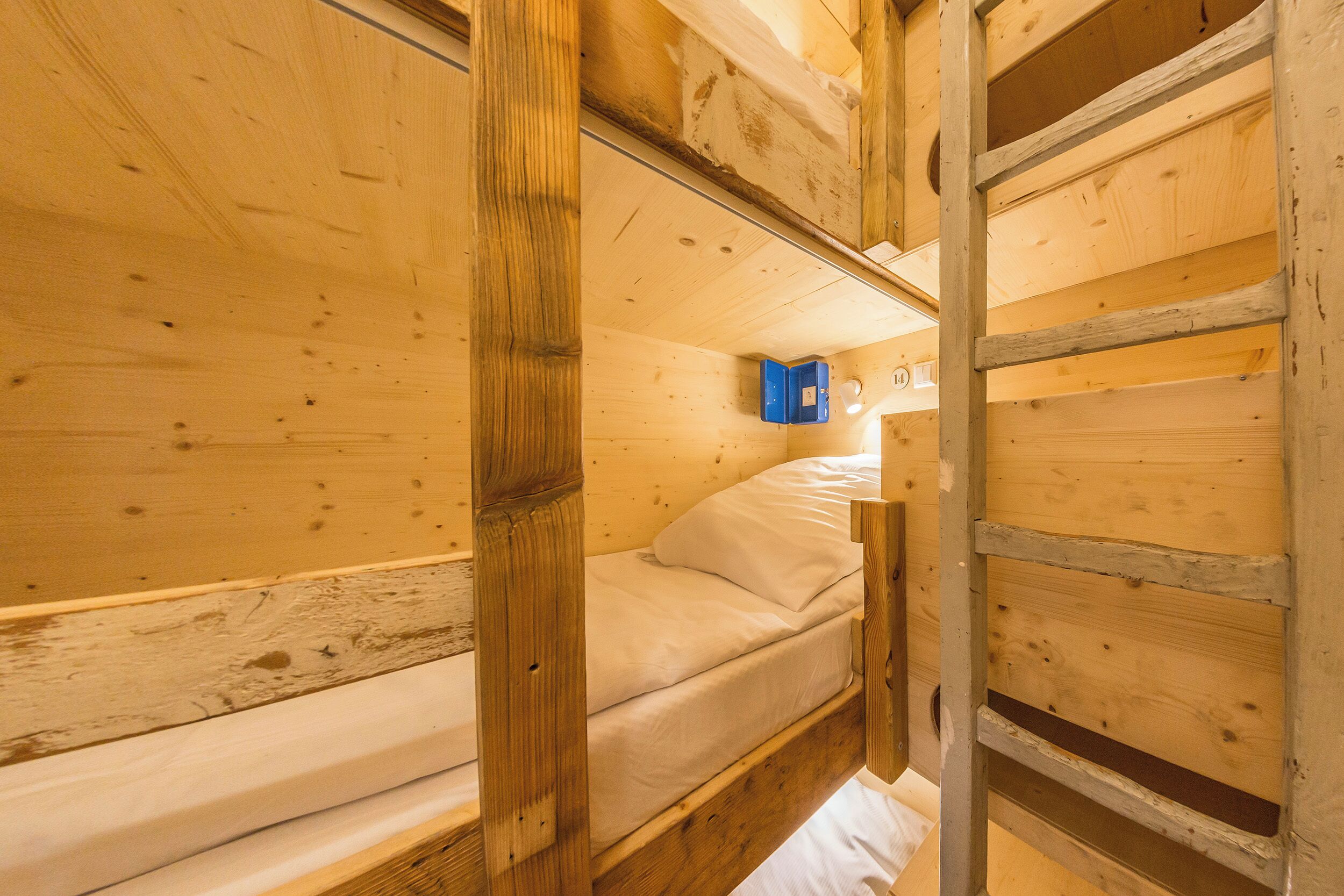 Ein Zimmer mit einem hölzernen Etagenbett, einer Leiter und einem blauen Staufach.