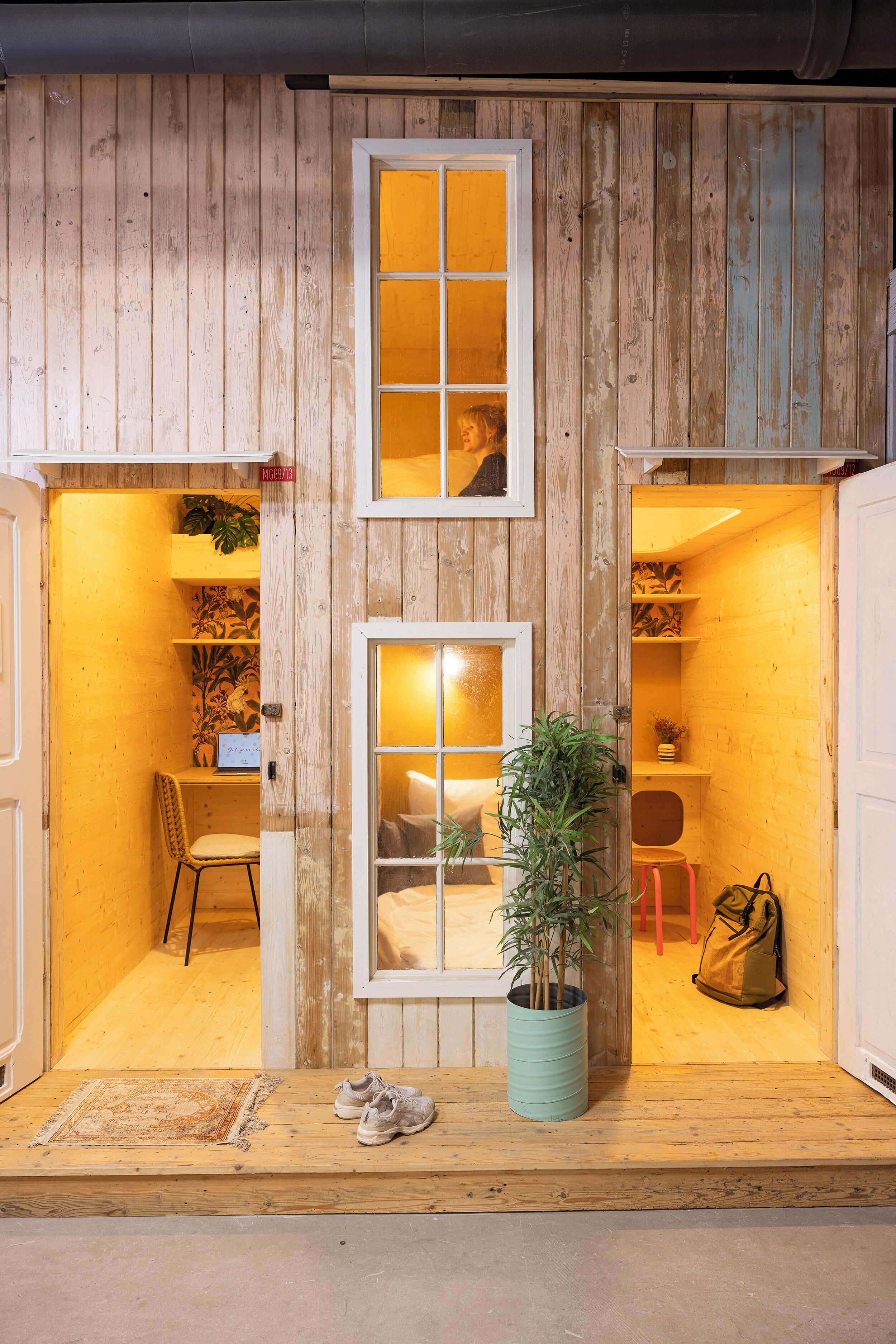 Un intérieur en bois avec deux fenêtres, un banc, une chaise, une plante en pot et un sac.