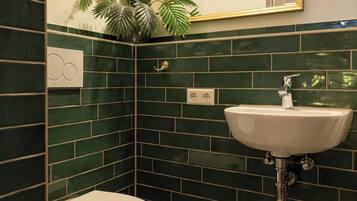 A bathroom with a white toilet, green-tiled walls, a white sink, and a mirror with a gold frame.