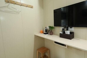 A small, clean room with a TV, a kettle, a cup, a plant, and a small stool. - Kunxin Hostel (Shanghai)